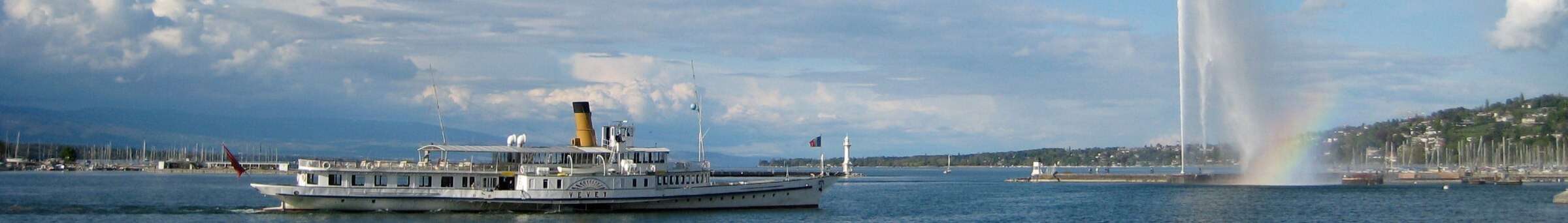A paddle steamer on Lake Geneva with the Jet d'Eau and a rainbow behind it